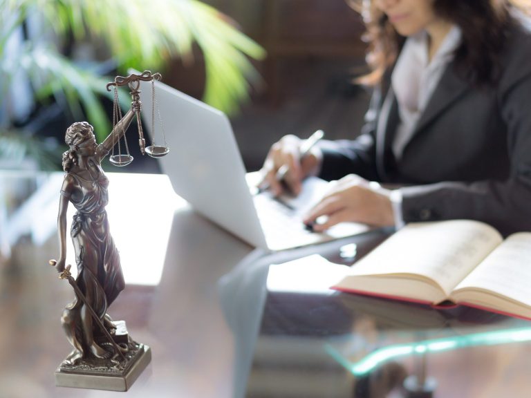 contrattualistica Statua della giustizia accanto a una persona che scrive al computer e consulta un libro.