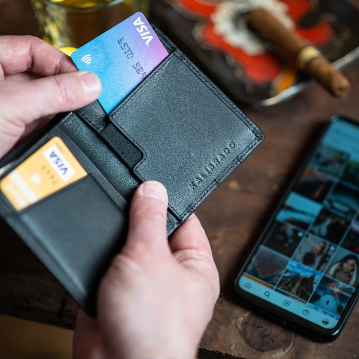image Black wallet holding credit cards, with a smartphone and a cigar in the background.