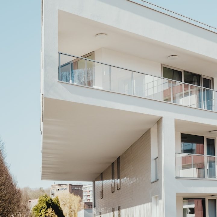 condominiale Modern building with a cantilevered upper floor and balcony, set against a clear sky.